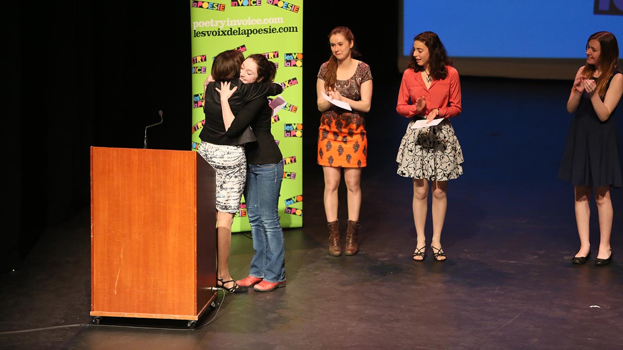 Kelsi James de Dr. Charles Best Secondary School (Coquitlam, C.-B.) a gagné le grand prix de récitation de la section bilingue en 2014. La voici en compagnie de Johanne Blais, qui la félicite, avec Marianne Verville, Andrea Rodriguez-Marin et Madina Sutton à ses côtés.  